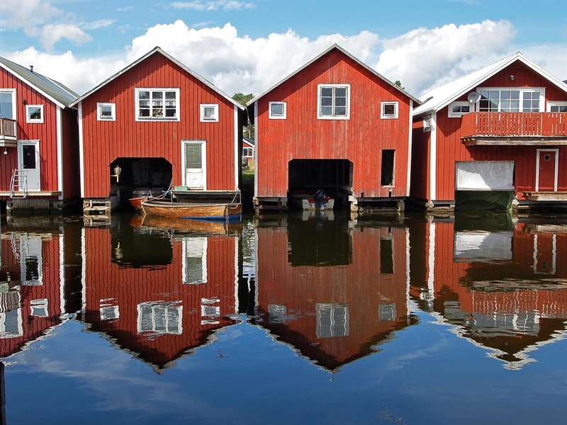 röda båthus på rad vid fiskeläge, blå himmel och spegelblankt vatten