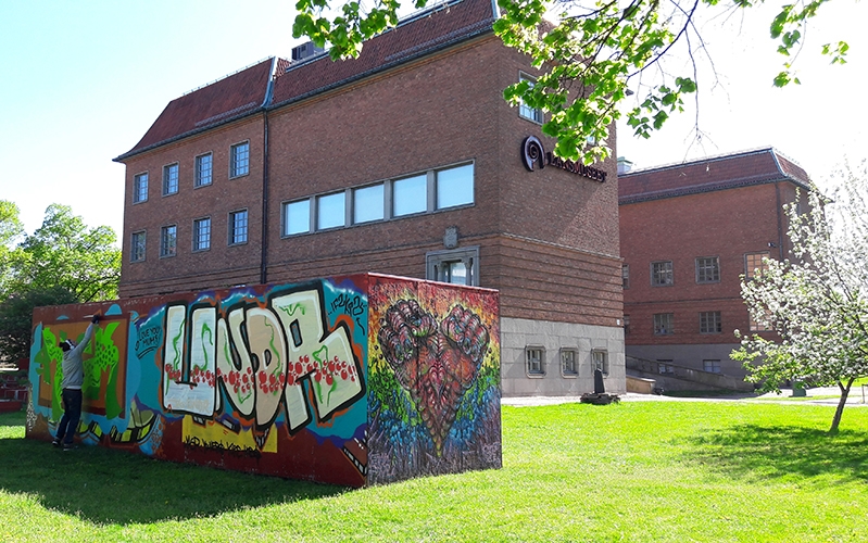 Grafittivägg och museets tegelbyggnad i solsken och grönskande gräs