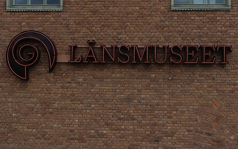 Länsmuseets logotyp som röd neonskylt på tegelfasad