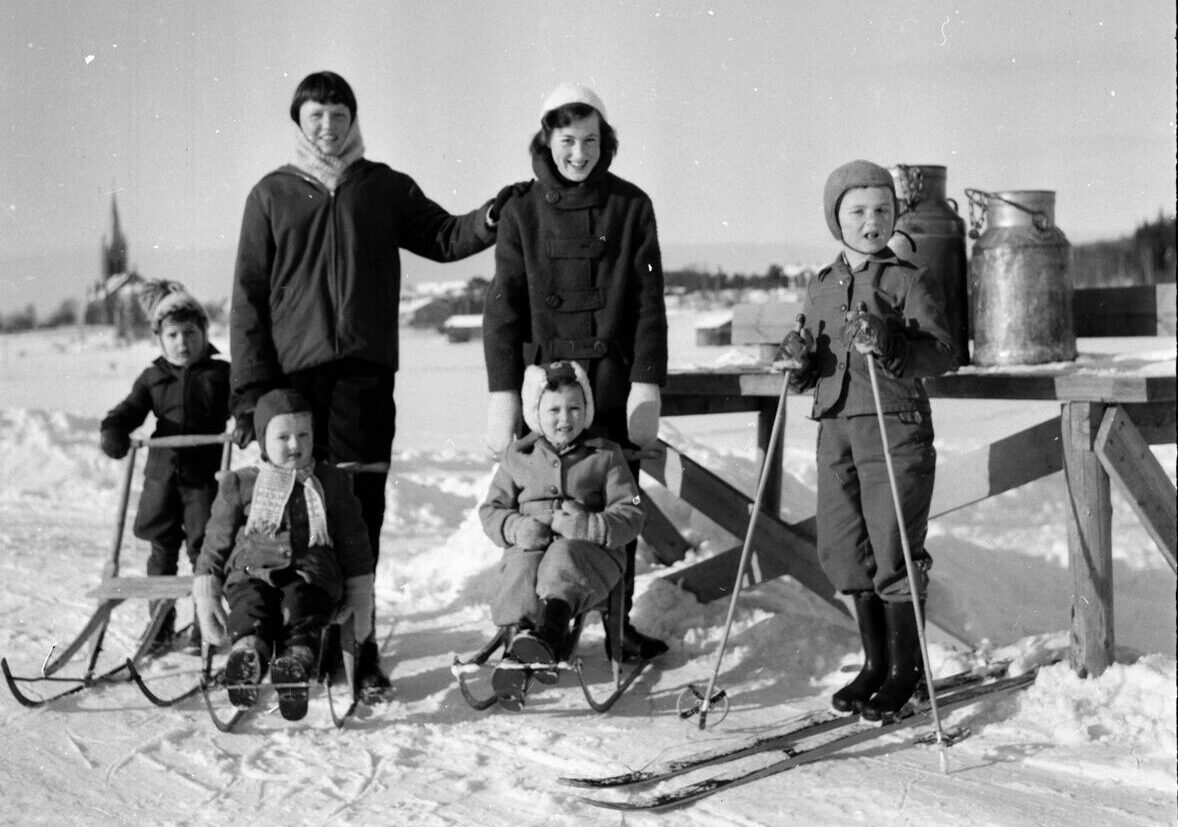 Barn och vuxna i vinterlandskap med sparkar och skidor.