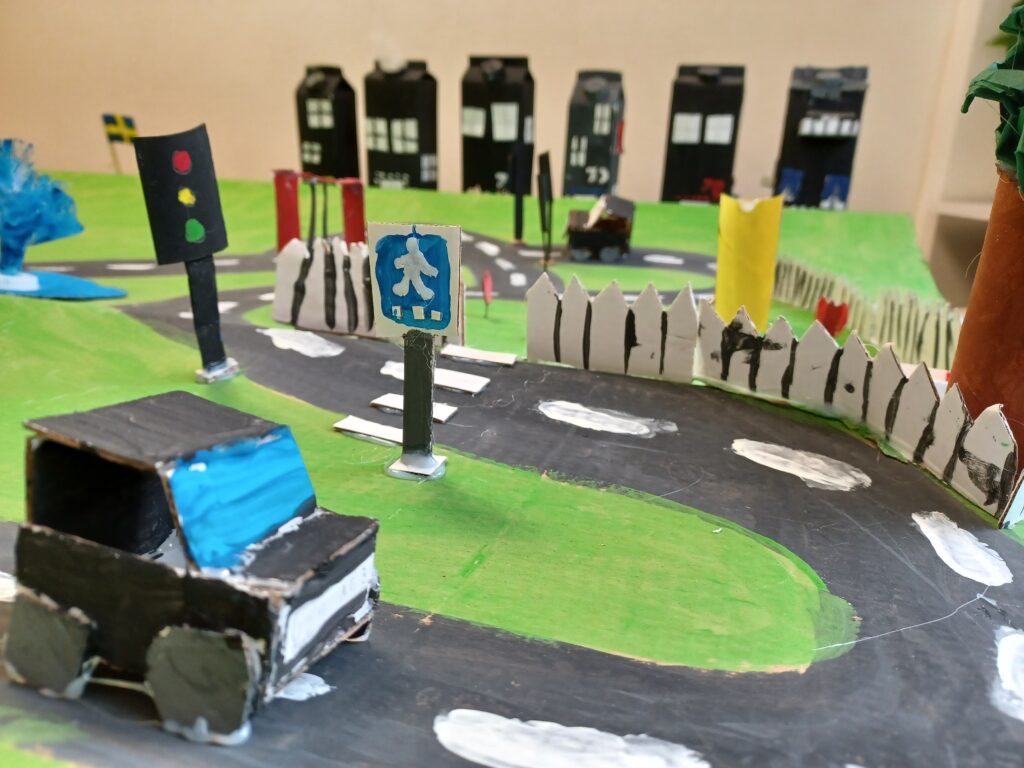 modell i kartong av en stad. en väg med en bil i kartong i förgrunden