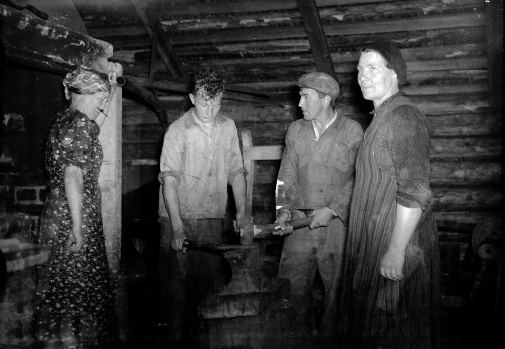 Ett svartvitt foto på två kvinnor och två män i en smedja.