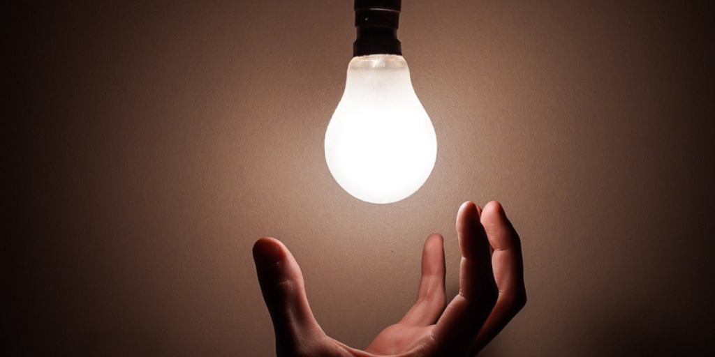 Bild på en glödlampa som lyser med en hand under den.
