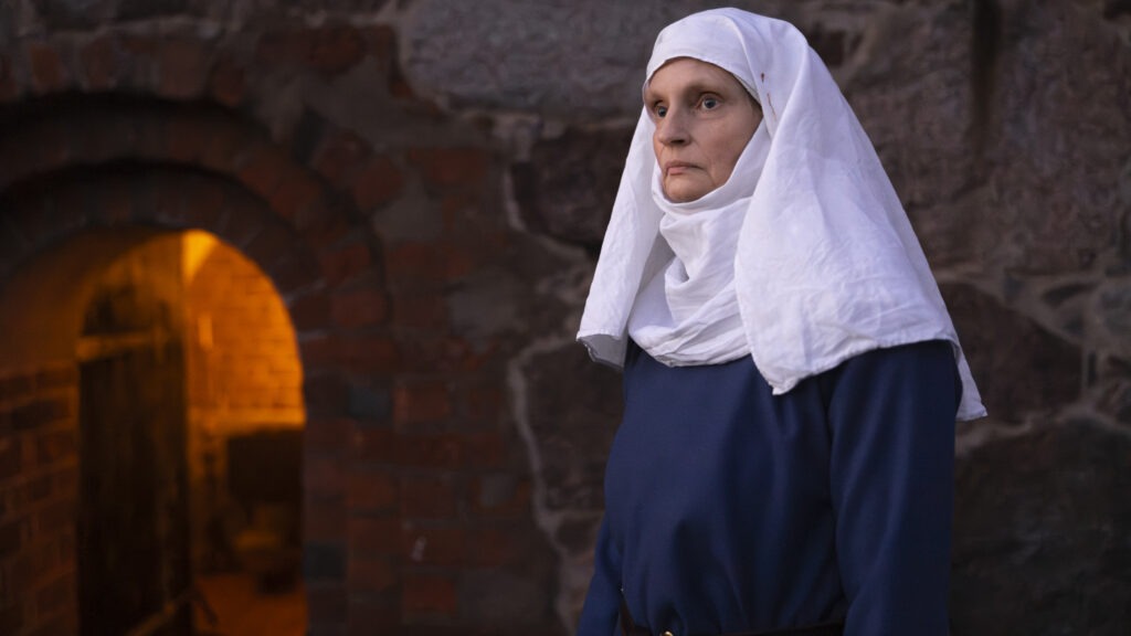 Föreställer en kvinna, som är nunna. Vid sjal och blå klänning